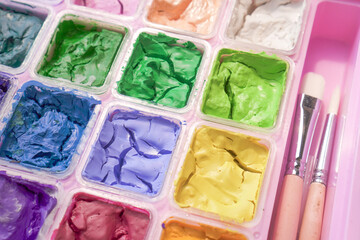 Dried colorful gouache in pink painting palette box with two pieces of white paint brush. Cracked water color and small brush.