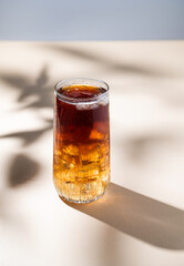 Long Island iced tea cocktail with hard liquor with rum, cola, lemon and ice on yellow background with shadow. The concept of a refreshing summer bar drink.