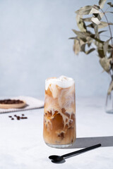 Iced coffee latte in a tall glass with milk on a light background with coffee beans, spoon and...