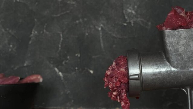 Close up of mincing beef meat with old manual meat grinder. Cooking meat for hamburger patties. Black concrete background