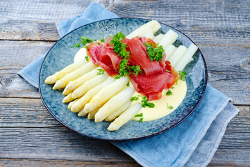 Traditional steamed white asparagus with cured ham with sauce hollandaise served as close-up on a Nordic design plate 