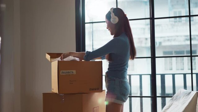 asian adult female relax unpack home relocation house renovation she is listening music while unpack her belonging stuff in a new apartment cheerful overjoy happiness expression home moving concept