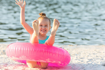 Happy joyful child girl in swimsuit having fun with swimming ring on a sand beach. Summer beach...