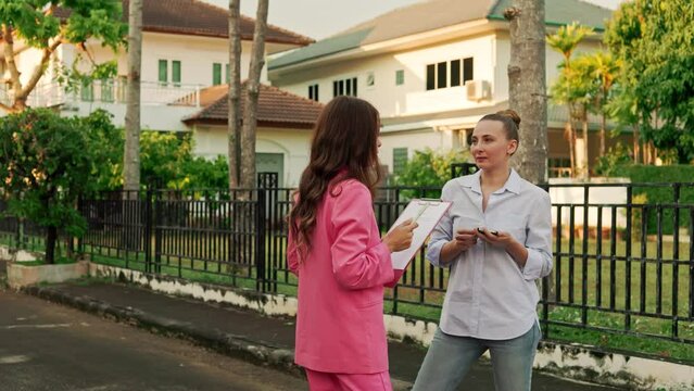 A real estate agent and her client are chatting and sharing jokes in front of houses located in an upscale residential area