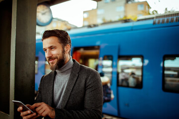 Young man using a smart phone while waiting for his train at the train station