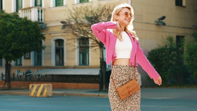 Young beautiful smiling model in trendy summer pink jacket clothes and skirt. Blond modern carefree business woman posing in the street at sunset. Positive blond female. Cheerful and happy