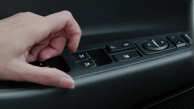 female hand turns on the car window control button on the door.