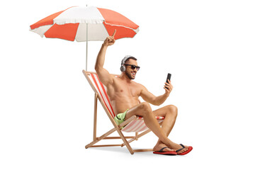 Young man in swimwear sitting on a beach chair and listening to music