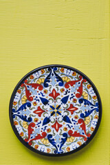 Assiette décorative en céramique colorée posée sur un mur jaune