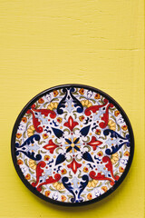 Obraz na płótnie Canvas Assiette décorative en céramique colorée posée sur un mur jaune