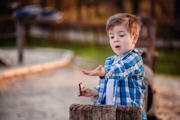Little toddler boy in blue shirt sitting on wooden train on playground, eating fruit bar. Showing...