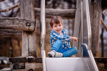 Little toddler boy in blue shirt trying to climb down a wooden ladder on playground
