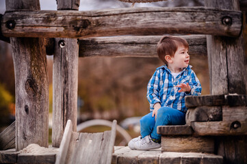 Little toddler boy in blue shirtsiting on a wooden stairs on playground