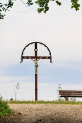 A field cross with depiction of the crucified Christ next to a rest bench on a field path near...