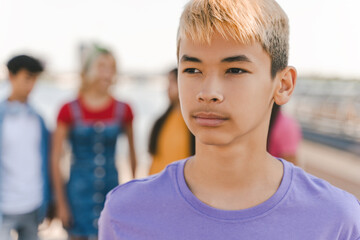 Portrait of pensive Korean teenage boy with colored hair wearing purple t shirt on street, outdoors