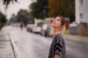 Close-up portrait of young woman with coloured blond hair in grey t-shirt standing on the street in the rain