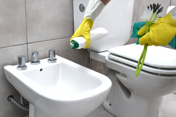 woman wearing gloves cleaning and disinfecting the toilet and bidet in a home bathroom