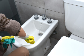 woman wearing gloves cleaning and disinfecting the toilet and bidet in a home bathroom