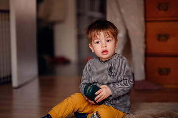Fototapeta premium Little thoughtful toddler boy sitting on floor playing with glasses case