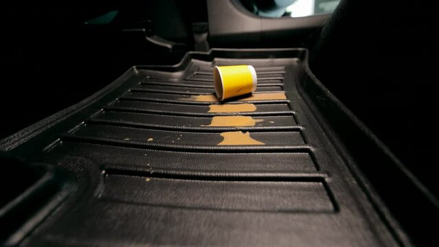 Pollution of the car in the cabin. a woman's hand drops a disposable paper cup onto the car floor mat. Spilled coffee on the carpet in the car.