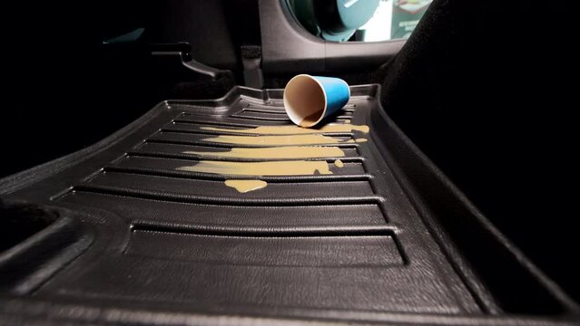 Spilled coffee on the carpet in the car. Pollution of the car in the cabin. A blue disposable cup with coffee falls on the car floor mat