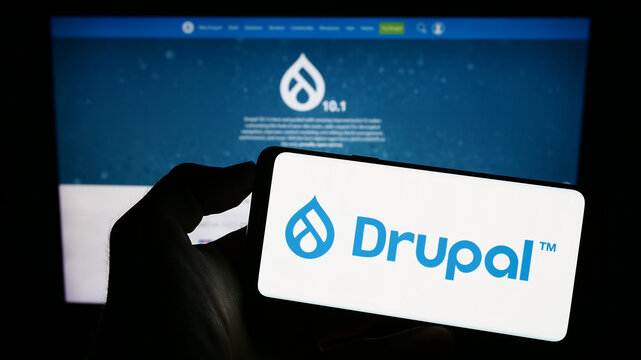 Stuttgart, Germany - 07-13-2023: Person holding cellphone with logo of content management system Drupal on screen in front of webpage. Focus on phone display.