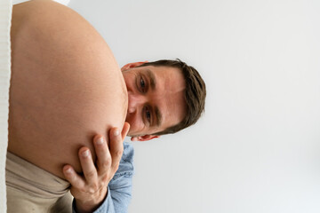 Happy father looking closely  on naked baby belly of standing expectant mother. Side view. White background. Bright shot.