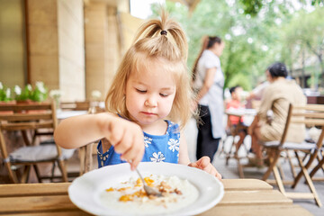 Little kid having breakfast at cafe. Adorable girl drinking still water, eating rice porridge with mango. enjoying breakfast. 