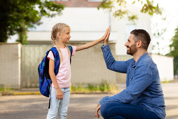 Father-daughter bonding. Parent and pupil of primary school giving high five and smiling at each...