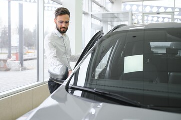 Naklejka na ściany i meble Happy young guy checking new luxury car, buying automobile at dealership centre. Portrait of cheerful millennial Caucasian man examining auto at showroom store