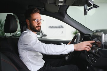 Happy caucasian man in formal wear getting inside luxury modern car for testing interior before purchase. Concept of dealership, selling and purchase