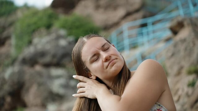 Against the backdrop of a blue staircase descending to the sea along the cliff, a young woman combs her wet hair. Slow motion.