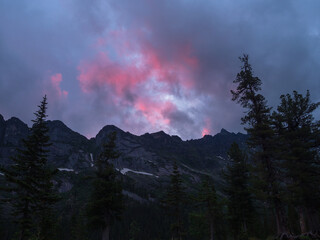 Dark silhouettes of mountains against a bright pink sunset sky. Red sunset over majestic mountains. Sunset in magenta tones. Atmospheric purple landscape with a high-altitude snowy mountain valley.