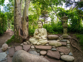 Stone Gautama Buddha decorative statue in a garden under green leaves. Outdoor Garden decor concept. Abakan