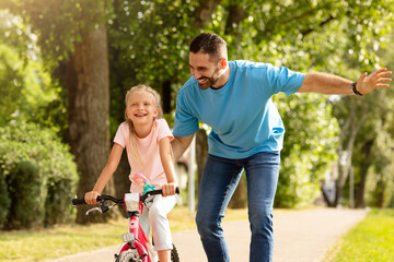 Outdoors activities. Happy father teaching his daughter to ride a bike in the park, enjoying time together on weekend