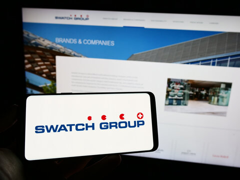 Stuttgart, Germany - 07-15-2023: Person holding cellphone with logo of Swiss company The Swatch Group Ltd. on screen in front of business webpage. Focus on phone display.