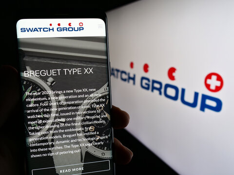 Stuttgart, Germany - 07-15-2023: Person holding mobile phone with website of Swiss company The Swatch Group Ltd. on screen in front of logo. Focus on center of phone display.