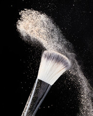 Two professional black makeup brushes with beige powder in motion and loose powder particles...
