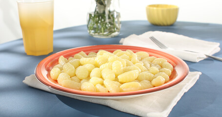Potato gnocchi on a red plate on a blue background. Close-up. Angle view. Camera tracking. Italian cuisine. Cooked food. Sunny day.