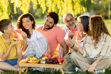 Glad european multi-generation family, enjoy picnic, fruits, eat watermelon in park