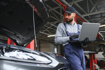 Smiling mechanic using a laptop pc at the repair garage.