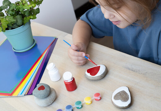 Child craft activities, girl paints heart on stones.Preschooler art work.Medical heart health concept, Mother's day handmade present.