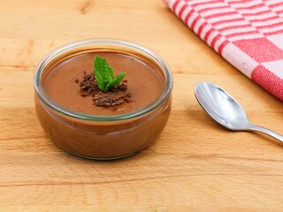 Delicious chocolate mousse finished with a mint leaf. Dessert with spoon and towel on a wooden background.