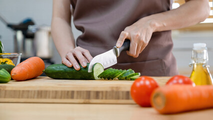 Woman cutting vegetables, cucumber ready for cooking.