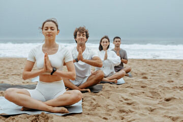 The beachside lotus. Young people meditating together during yoga lesson outdoors, sitting on mats on the beach