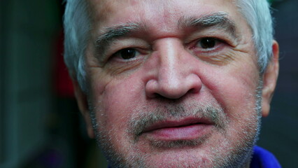 Close-up face of a mature unshaven senior man with gray hair and wrinkles staring at camera in macro portrait displaying old age experience