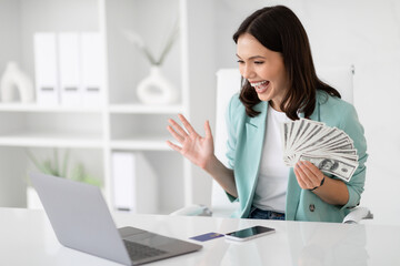 Surprised glad millennial caucasian lady in suit hold lot of cash, enjoy success, celebrate win, look at laptop