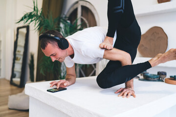 Smiling man in headphones with smartphone doing yoga