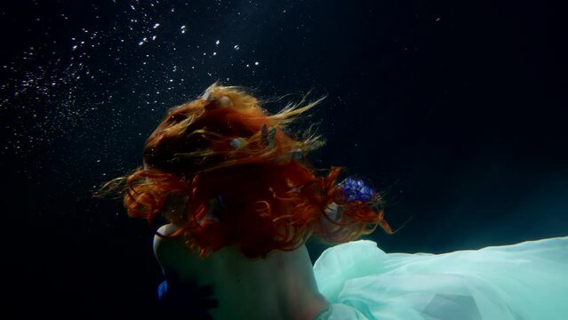 dream and fantasy underwater, mysterious female figure in dark depth, rear view of beautiful woman