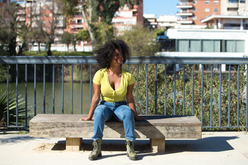 Young and beautiful black woman with afro hair dressed in jeans and yellow shirt sitting on a...